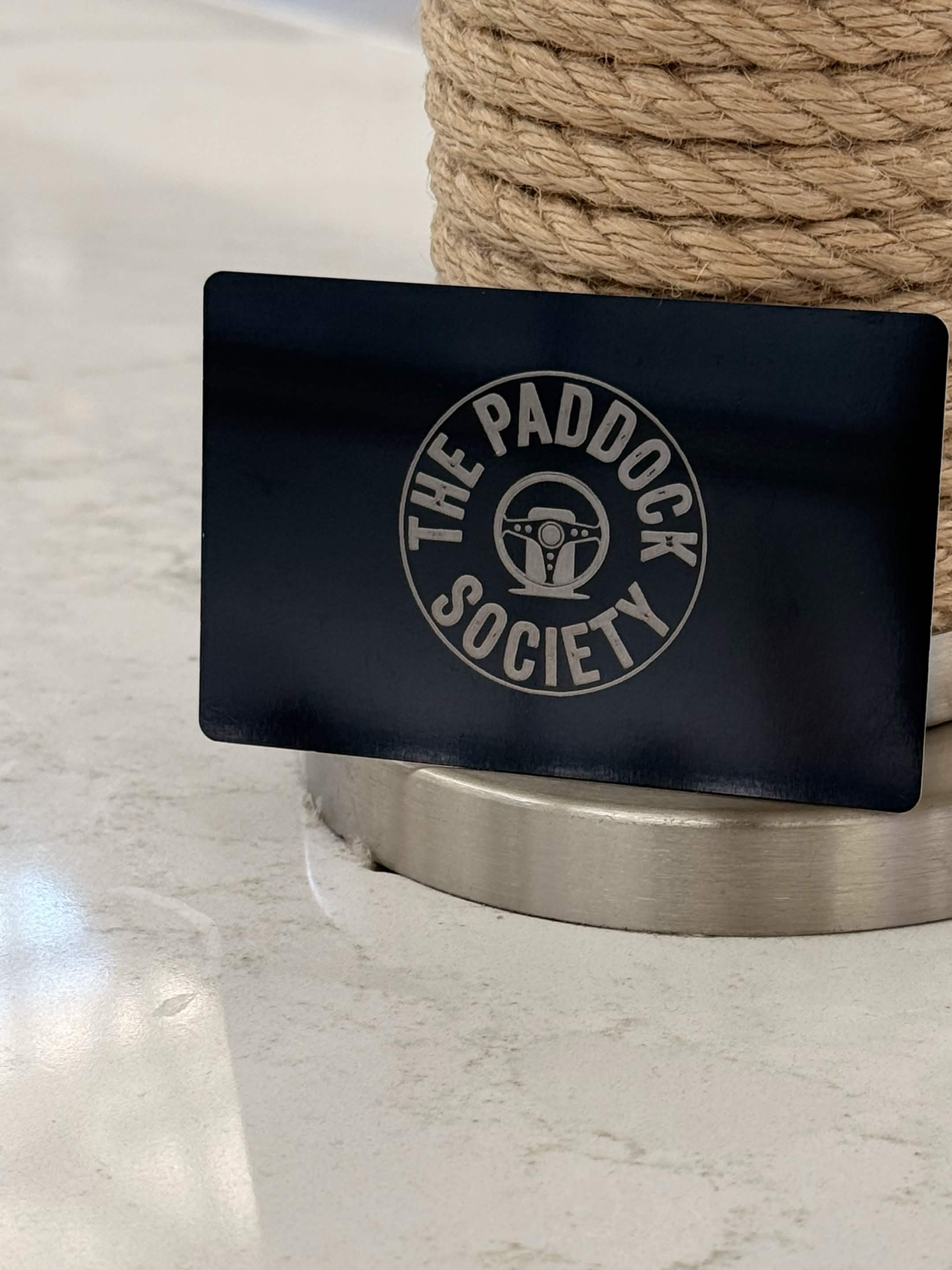 A Paddock Society card propped against a rope post in an airline lounge